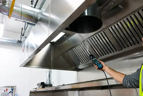 Engineer measuring kitchen hood motor airflow using a digital anemometer